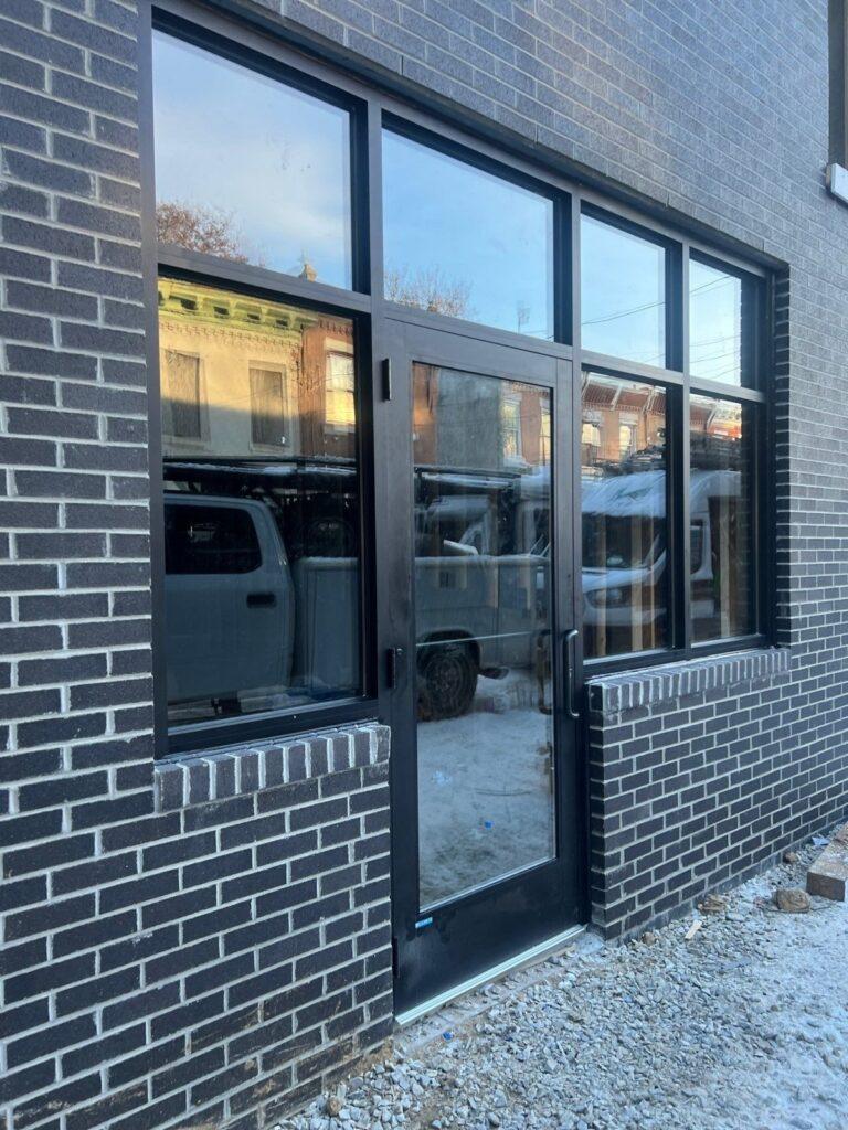 Black aluminum storefront windows and door in a dark brick facade