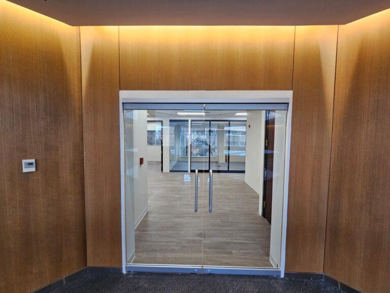 Frameless glass double entry doors in a wood-paneled lobby by Pexic Windows