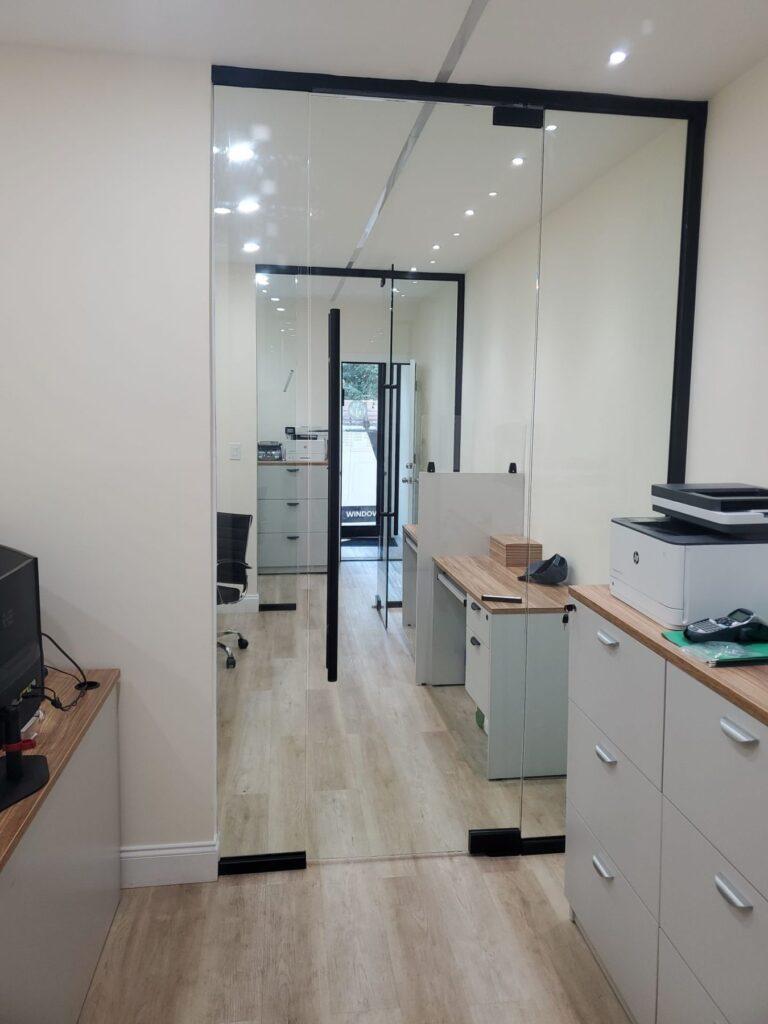 Frameless glass office wall and pivot door with black trim by Pexic Windows